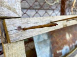 A large long rusty old iron metal construction industrial nail sticks out of a wooden plank photo