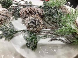 Christmas mock up, grey ceramic or clay plate top view for text or design, spruce or pine branch covered in snow and cones on a wooden rustic table photo