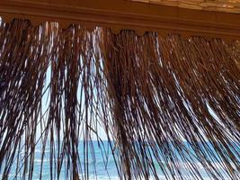 View of the blue sea with salt water through the yellow dry straw of the sun umbrella on the beach in the warm eastern tropical country southern paradise resort. The background photo