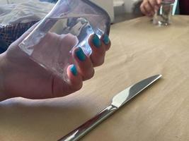 Healthy lifestyle. Caucasian young woman drinks a glass of water while sitting at cafe. Beautiful healthy woman follow healthy lifestyle. the manicured hands with black glitter nails photo