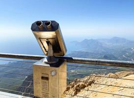 binoculars on an observation deck made of gray metal. sightseeing tour, observation of the view from the mountains down. next to the binoculars, a protective fence for tourists photo