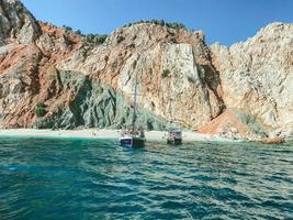 roca en el centro del mar. agua azul con espuma burbujeante con una gran montaña alta en el centro. barcos con turistas junto a la roca. en barcos de velas altas y fósforos foto