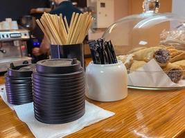 mesa de centro. cafetería con mostrador de autoservicio. azúcar, especias, espátulas de madera para mezclar la bebida se colocan sobre la mesa. en un plato túbulo de postre dulce con chocolate foto