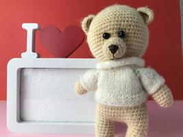 soft knitted bear on a red background with a cute frame in white. romantic sentimental gift for a girl. cute photo frame and teddy bear for baby