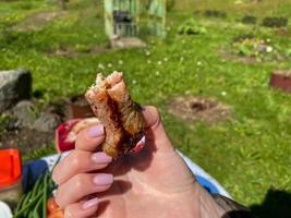 In the hands of a woman's girl in her hand, a fried piece of pork kebab cooked on a fire on a smoke, delicious photo