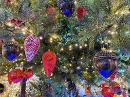 Green branches of a fluffy Christmas festive New Year tree with toys in balls and bright glowing light bulbs and garlands, background photo