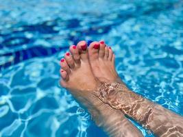 pies desnudos de mujer sobre el agua azul de la piscina foto