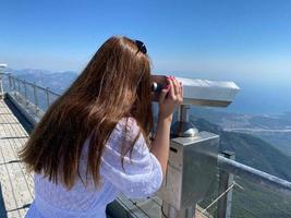 Woman tourist looking at the cloudy mountains through telescope photo