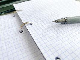 a sheet of white paper in a cage from a notebook. diary to record all personal affairs and tasks. retro notepad with black ballpoint pen and metal rings photo