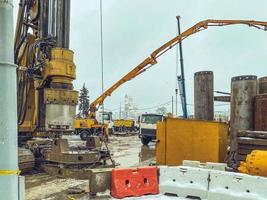 construcción de un nuevo puente en el centro de la ciudad. el equipo funciona en invierno en la nieve. Grúa grande y pesada transfiere hormigón. el sitio está cercado con conos de plástico de personas y automóviles foto