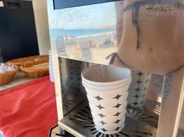 Water is poured into a disposable paper cup for drinking from a cooler with water and drinks, close-up view. Faucet for pouring drinks photo