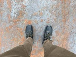 Legs of a man in boots on the background of a rusty old iron red scratched metal corrosed sheet surface background, texture industrial in loft style photo