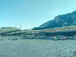 hot, tropical country with sea and mountains. on the beach there are pebbles and small stones. under a stretched awning there are multi-colored soft sunbeds photo