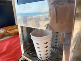 Water is poured into a disposable paper cup for drinking from a cooler with water and drinks, close-up view. Faucet for pouring drinks photo