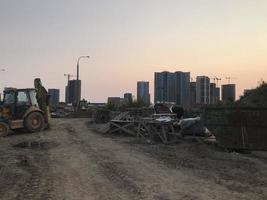 una pavimentadora de asfalto está conduciendo contra el telón de fondo de nuevas casas en el microdistrito. el tractor va al sitio de construcción y lleva residuos de construcción foto