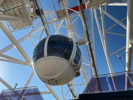 A large Ferris wheel against a blue sky. Booths with people go up photo