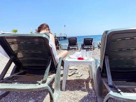 vacation by the sea. there are sun loungers on the shore, a girl in a red bikini with dark hair sits on them. sea voyage, sunbathing photo