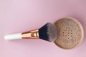 loose powder on a bright background. powder with white handle and gold nap holder. brush made of natural materials. powder with a pink tone photo