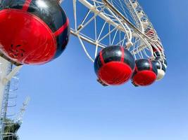 amusement park. Ferris wheel made of white metal. On the wheel there are large cabins for riding red tourists photo