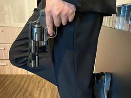 Close up on hand of unknown caucasian man holding a gun in by his leg while standing outdoor in sunny day - handgun criminal or self-defense concept with copy space photo