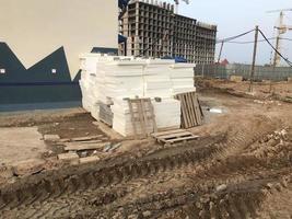 dirt at a construction site. sand furrows, tracks from heavy vehicles. next to it are building materials, polystyrene, wooden pallets. against the background of houses under construction, high cranes photo