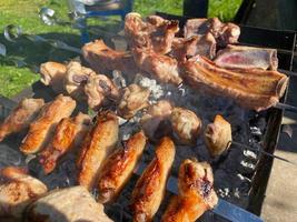 Delicious beautiful fried kebab of pork meat, chicken wings and pork ribs on the smoke cooked on the grill with skewers with coals. Barbecue in nature. BBQ photo