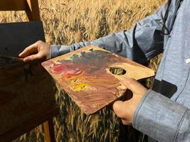 The artist holds a paintbrush in his hand, with which he mixes bright watercolor paints on the palette. The creative process. The art of drawing. Inspiration photo