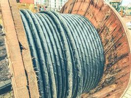 carrete de madera en un sitio de construcción. un cable negro y largo se enrolla en la bobina para crear comunicaciones. cables para tender en un nuevo microdistrito foto