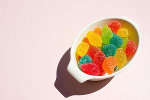 Colorful sweet jelly in white bowl on pink background with free place for text,harmful snack for kids,plate full of multi-colored candies,horizontal image for banner,design with copyspace,top view photo