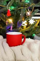 Blank red mug with christmas tree on background,mat tea or coffee cup with christmas and new year decoration,horizontal mock up with ceramic mug for hot drinks,empty gift print template. photo