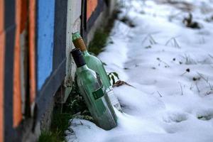 Two green glass empty alcohol bottles standing in snow near kiosk wall photo