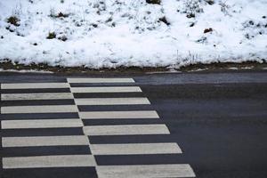 Road crossing zebra on black wet asphalt road with snow covered sides low angle view photo