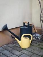 Two watering cans standing in a corner of a concrete building on tiled pavement photo