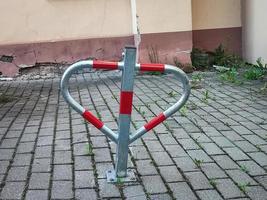 Parking prevention bollard with red parts standing on tiled ground surface in a yard near building corner with grass photo