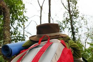 equipo para acampar: mochila, colchoneta, almohada y sombrero sobre un fondo de bosque. foto
