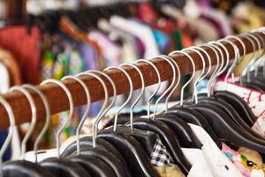 Wooden clothes racks with hangers and with colorful clothes on a blurred background inside shop. photo