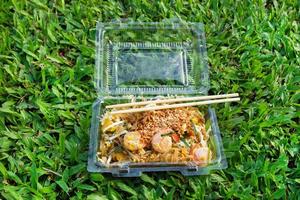 Noodles with vegetables, shrimps and eggs - Pad thai - in a plastic container on a grass Thai street food. photo