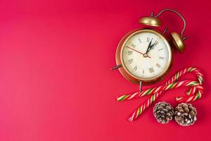 despertador de bronce, bastón de caramelo y conos de abeto sobre fondo rojo. fondo de navidad y año nuevo foto