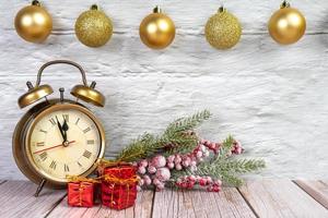 Decorative christmas tree, gift boxes and alarm clock on white wooden background.
