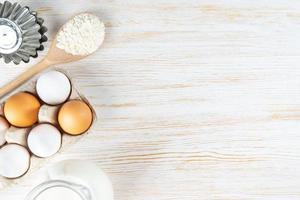 Baking ingredients flour, eggs, milk, bakeware on white wooden background with copy space photo