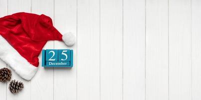 sombrero rojo de santa claus y calendario perpetuo azul sobre fondo blanco de madera foto