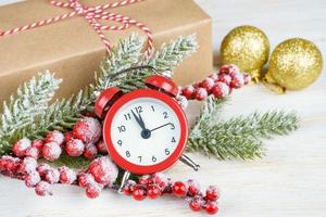 Christmas snow fir tree, alarm clock and gift box on white wooden background.