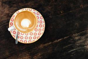 capuchino caliente en una taza blanca y roja sobre una mesa de madera en un café, vista superior. foto