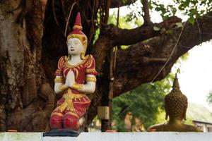 Small stone red and gold statue Buddha near to temple on a background of tree. Chiang Mai, Thailand. photo