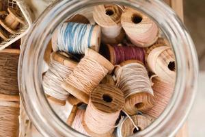 Top view on wooden coils with colorful threads in a glass jar. photo