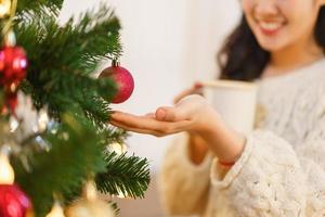 Christmas concept, Asian woman drinks coffee and touching red ball on christmas tree with happiness photo