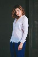 retrato de una joven y hermosa actriz triste con cabello castaño corto en camisa blanca y pantalones azules en el estudio foto