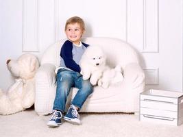 niño sonriente de tres años jugando con un cachorro blanco de samoyedo en el estudio foto