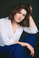 Portrait of young, beautiful sad actress with short brown hair in white shirt and blue pants in the studio photo