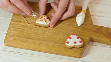 Process of decorating gingerbread with icing. Woman hands decorate cookies in the heart shape for Valentines Day video
